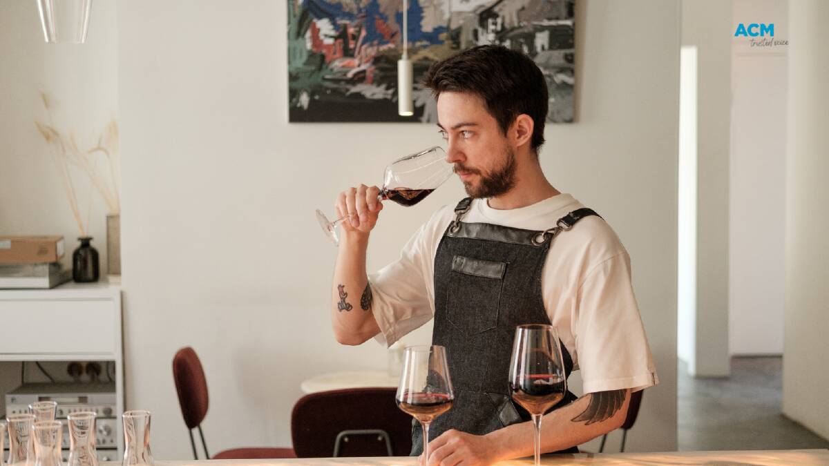 A bar worker smells red wines in the glass. Picture via Canva